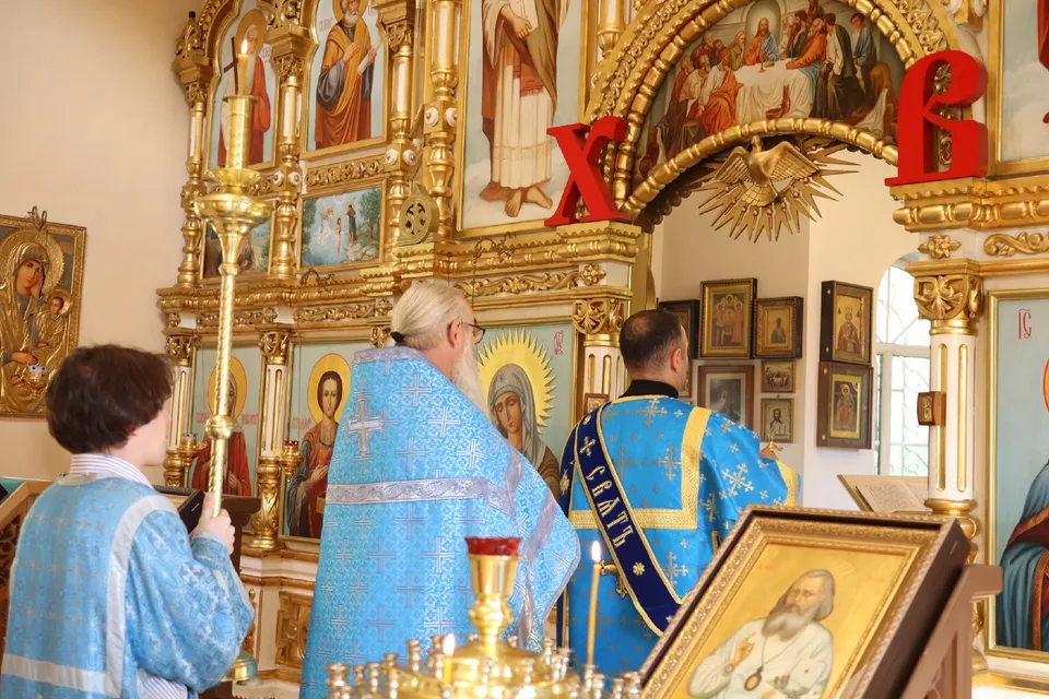 Три священнослужителя в голубых облачениях перед иконостасом внутри храма