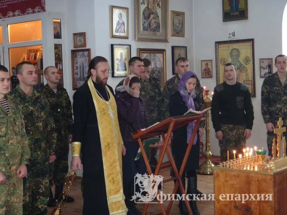 Священник в облачении читает молитву у аналоя, вокруг — военнослужащие в камуфляжной форме
