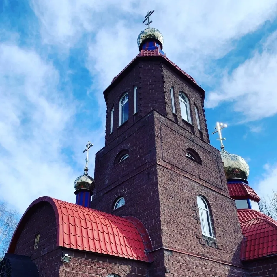 Вид снизу на шатровую колокольню и купола с крестами на фоне облачного неба